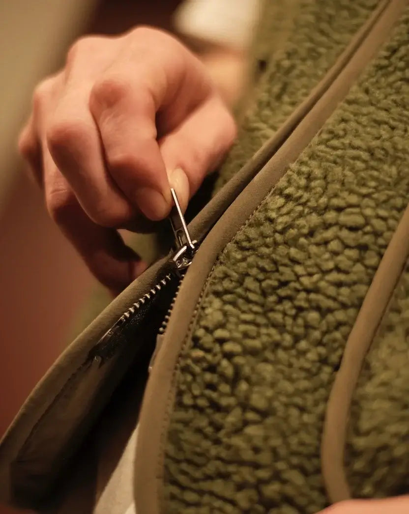 Detail van de groene bodywarmer van Wiggy's Supply met hand die de rits sluit.