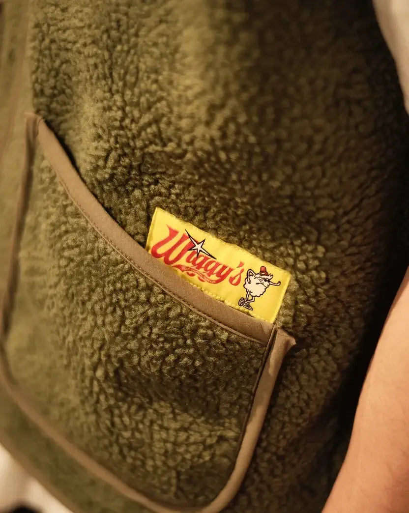 Detail van de Wiggy’s Supply bodywarmer in groen met logo op zak.